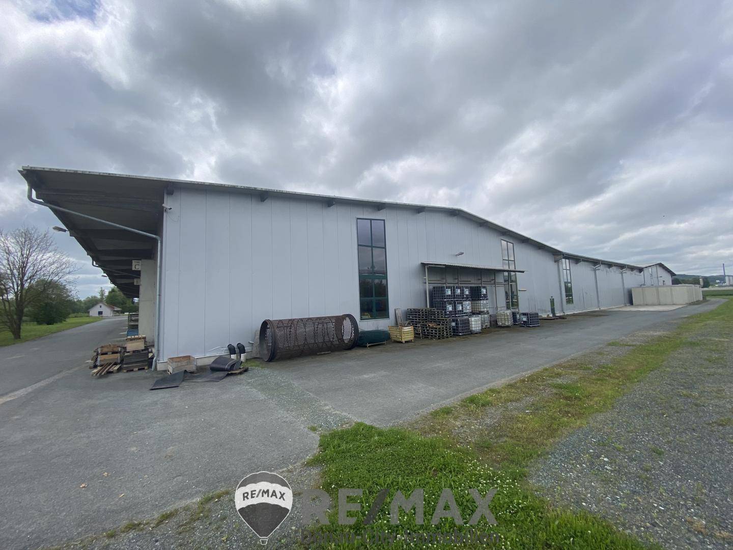 Seitenansicht eines Industriegebäudes mit großen Fenstern und einem Ladebereich mit Paletten und Materialien.