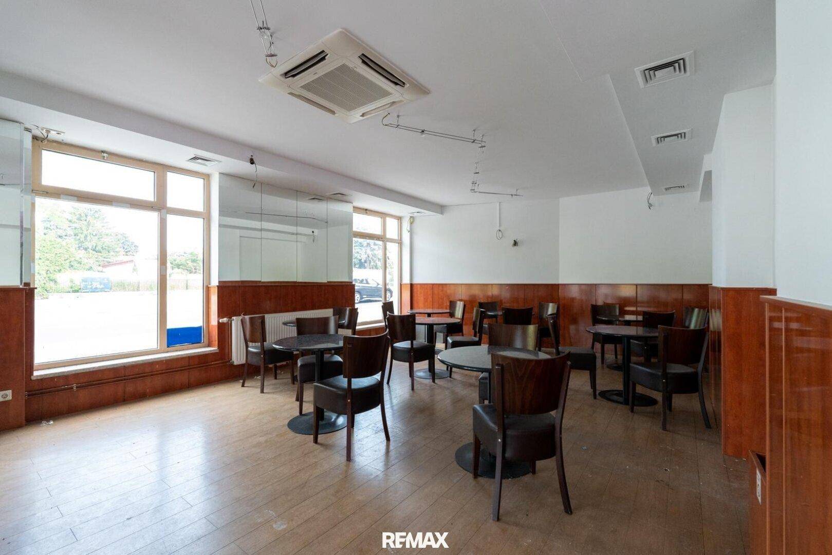 Großer Gewerberaum mit Holzboden, Tischen und Stühlen, ideal für ein Restaurant oder Café.