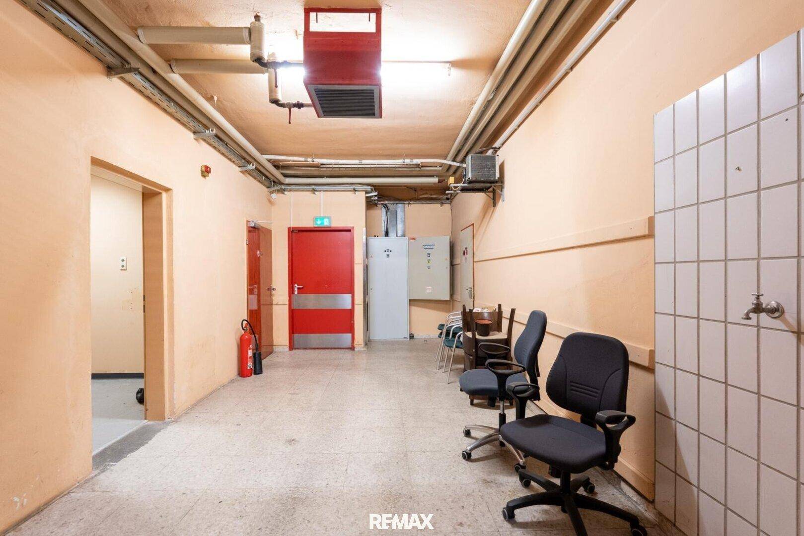 Langer Flur im hinteren Bereich des Gebäudes mit verschiedenen Installationen und Bürostühlen.