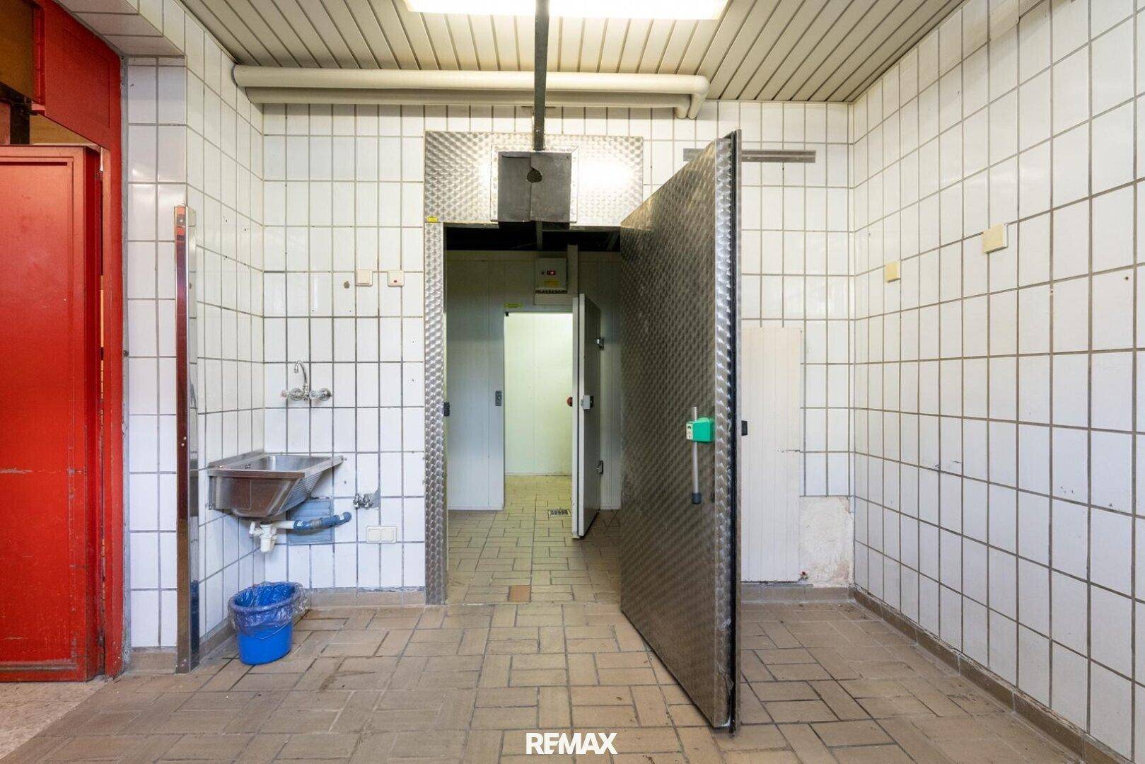 Funktionaler Wirtschaftsraum mit gefliesten Wänden, einem Waschbecken und einer großen Metalltür.