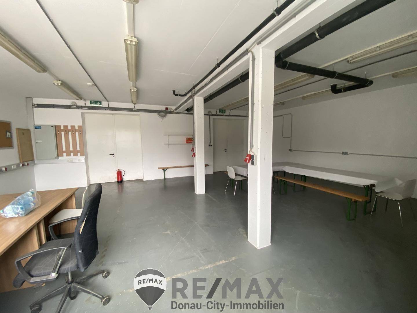 Aufenthaltsraum oder Gemeinschaftsbereich mit Tischen, Bänken und einem Schreibtisch, ausgestattet mit Betonboden.