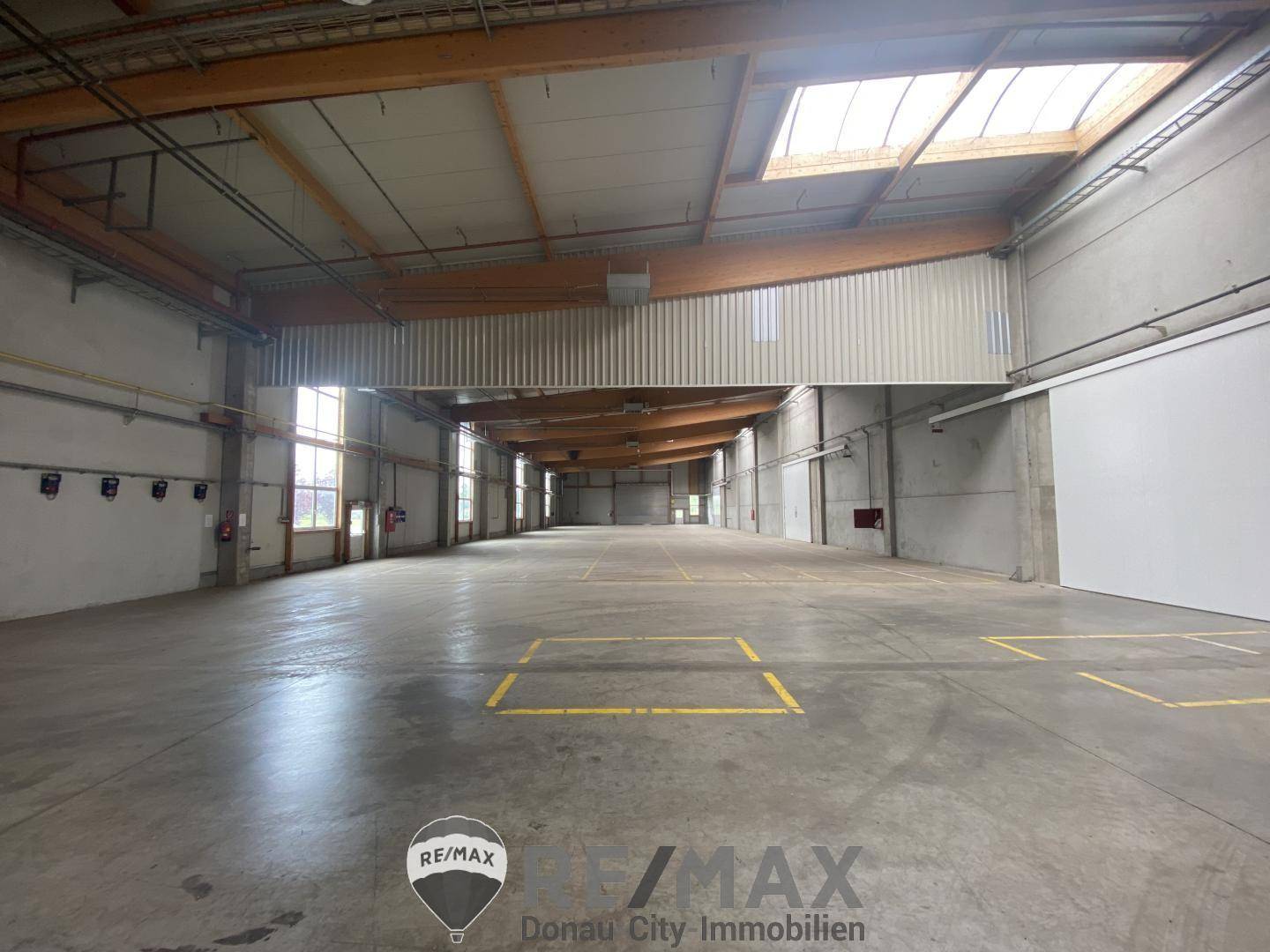 Geräumige, leere Lagerhalle mit hohen Decken, sichtbaren Holzbalken und Oberlichtern für natürliches Licht.