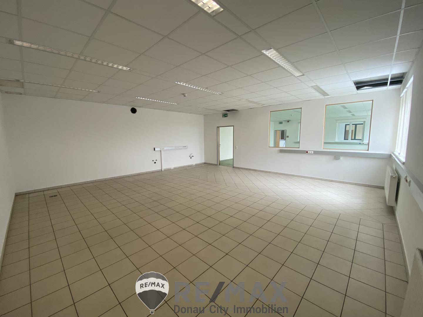 Großes, leeres Büro mit Fliesenboden und Fenstern, die einen Blick nach draußen ermöglichen.