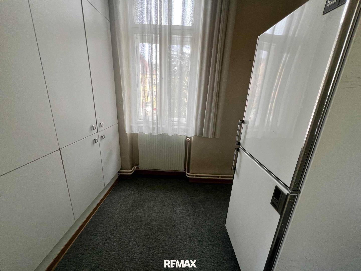 Kleiner Raum mit Teppichboden, Einbauschränken und einem Kühlschrank, der als Abstellraum dient.