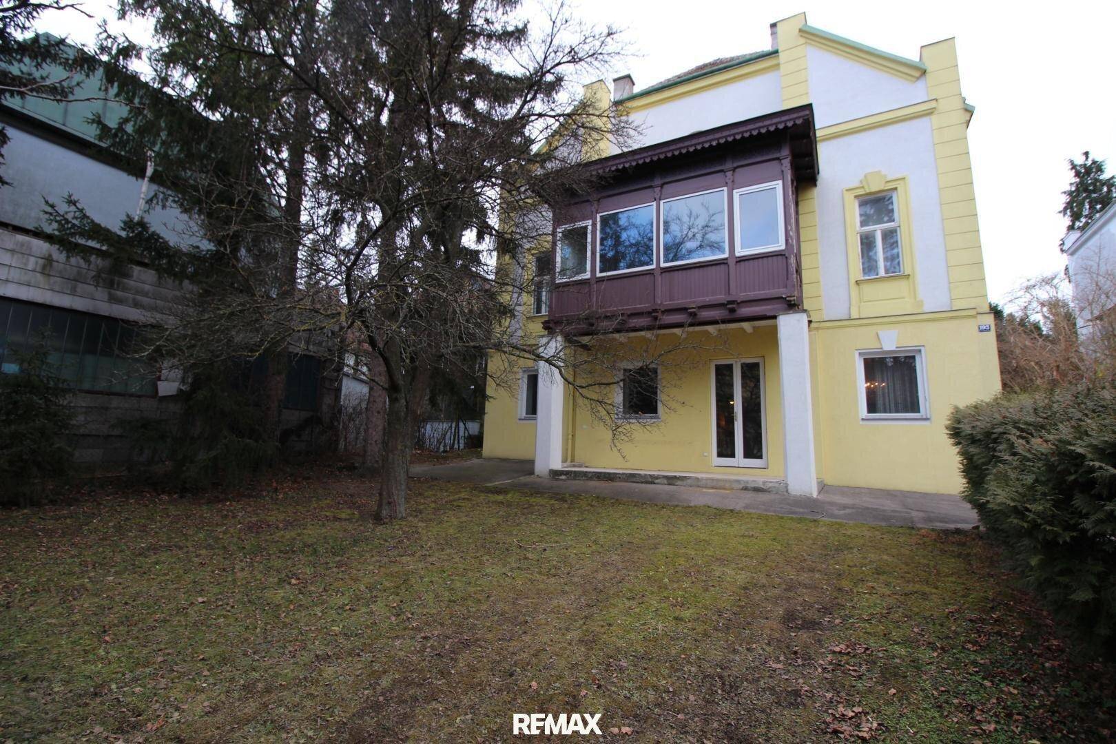 Rückansicht eines älteren Gebäudes mit gelber Fassade, Loggia und Gartenbereich.