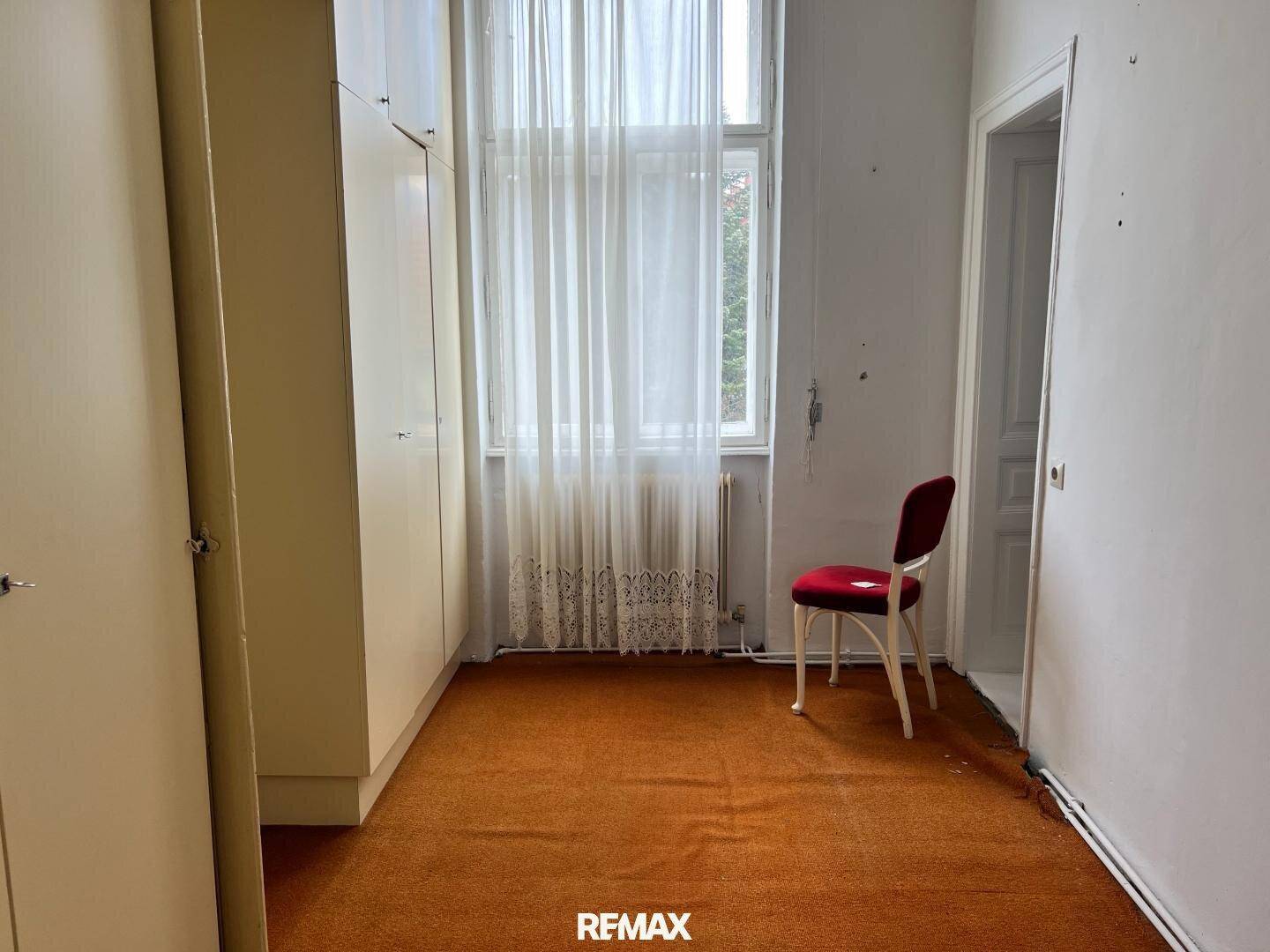 Schlafzimmer mit Teppichboden, Einbauschränken und einem großen Fenster mit Vorhängen.