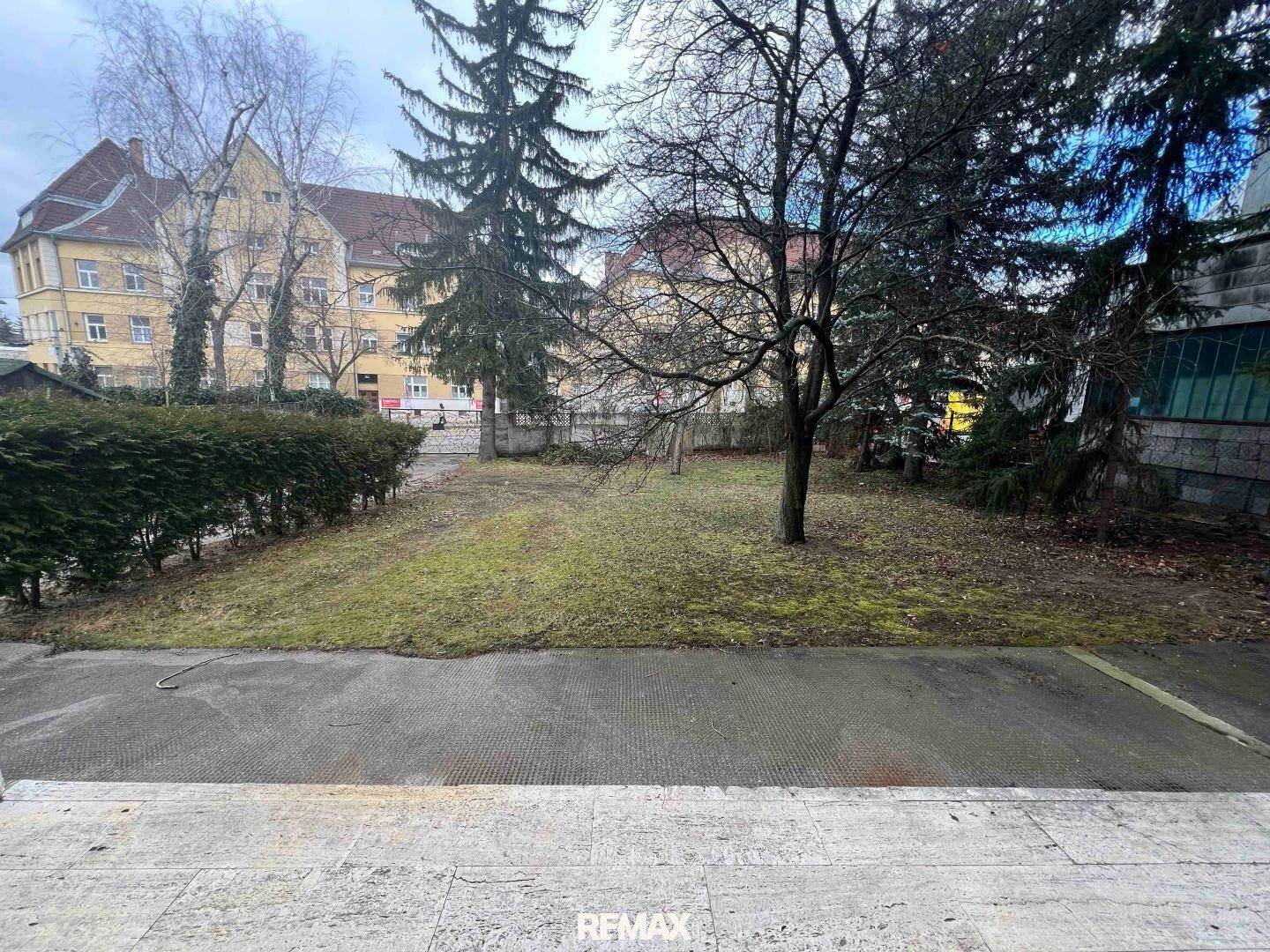 Großer Gartenbereich mit Rasenfläche, Bäumen und Blick auf umliegende Gebäude.