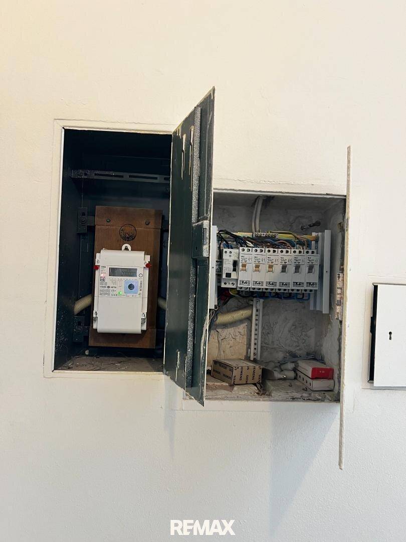 Offener Sicherungskasten und Stromzähler in einem Technikraum oder Flur.