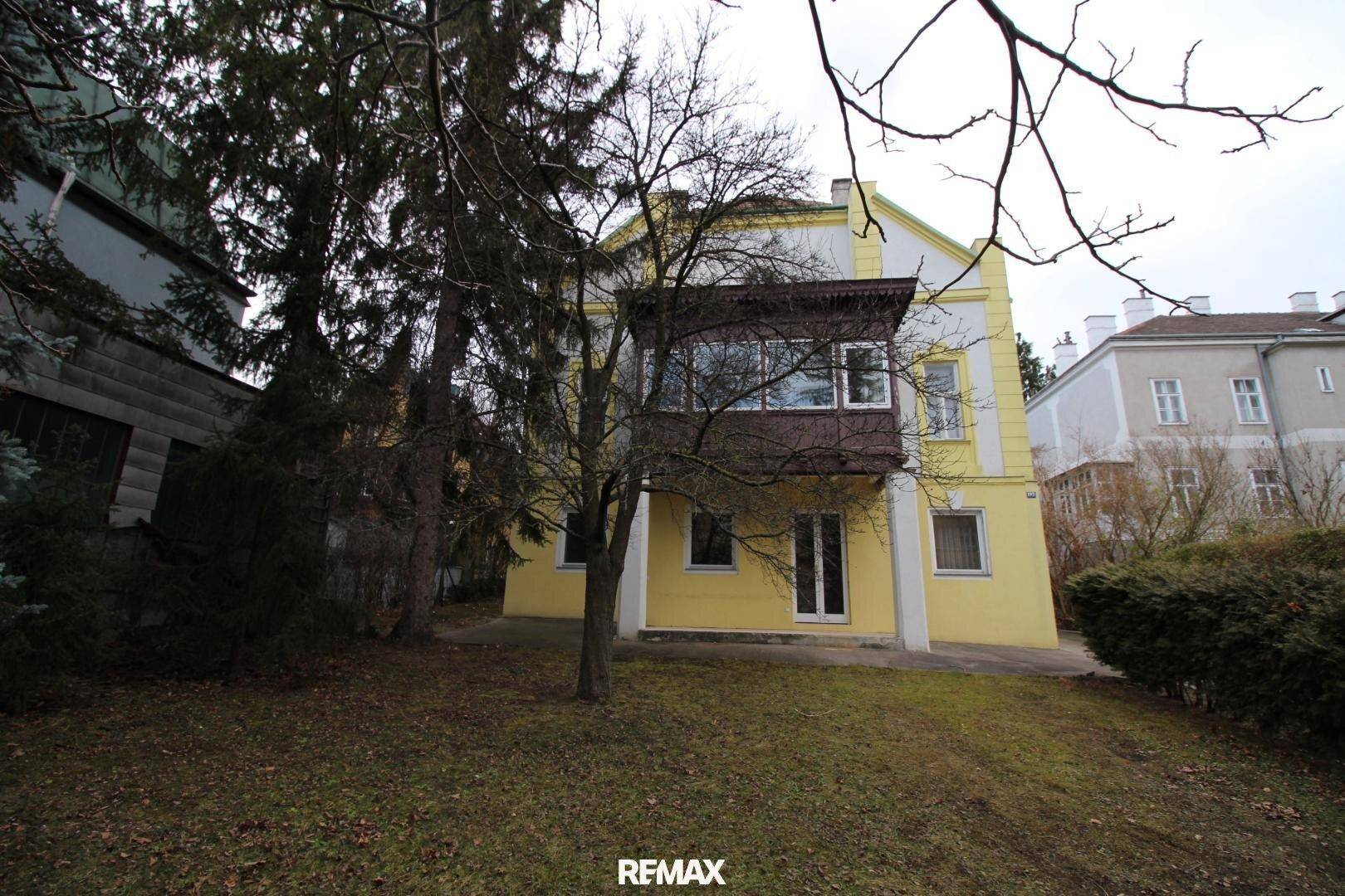 Rückseite der Villa mit einem gepflegten Garten und einem verglasten Anbau im Obergeschoss.