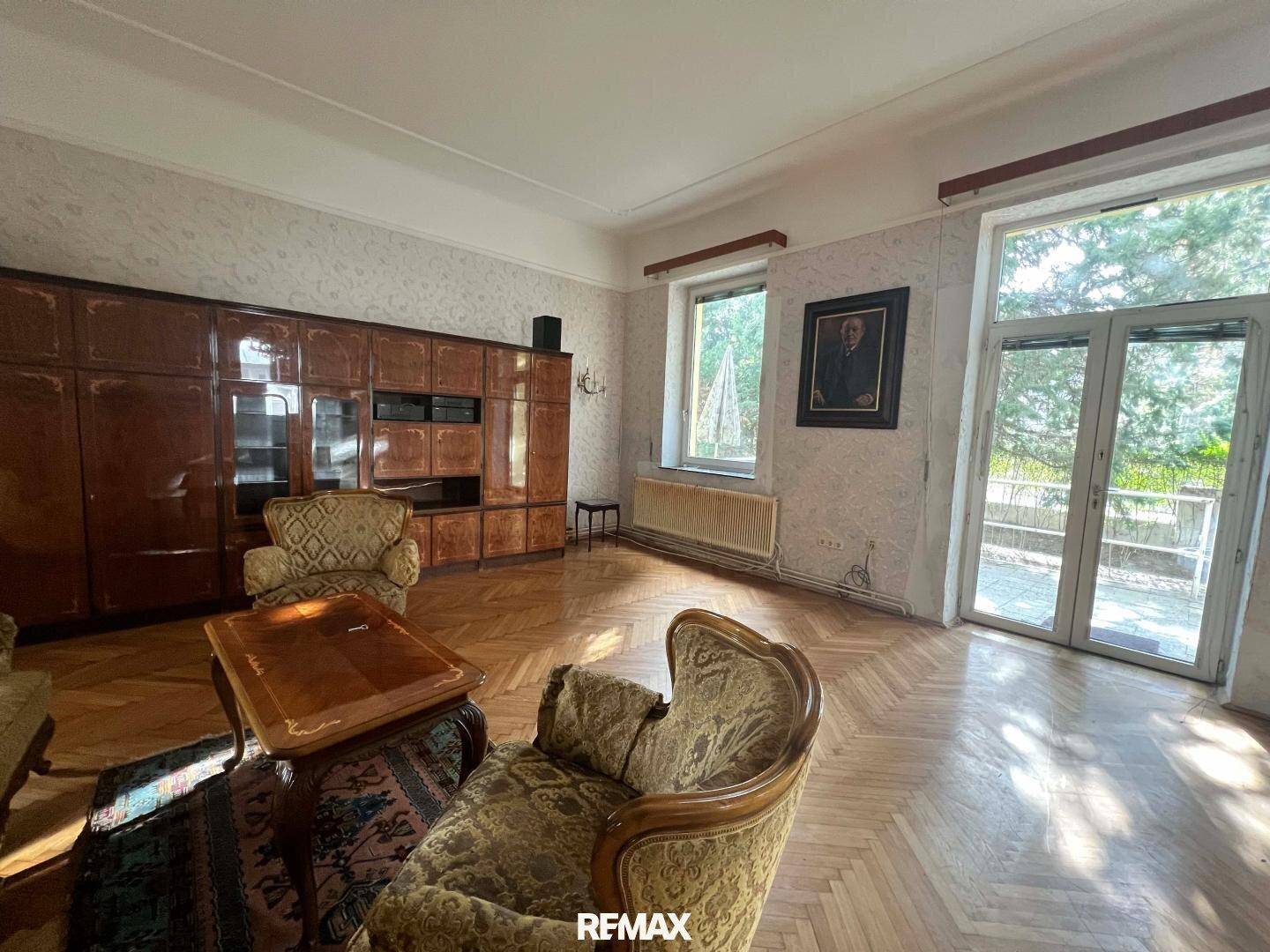 Klassisches Wohnzimmer mit Fischgrätparkett, traditionellen Möbeln und großen Fenstertüren zum Außenbereich.