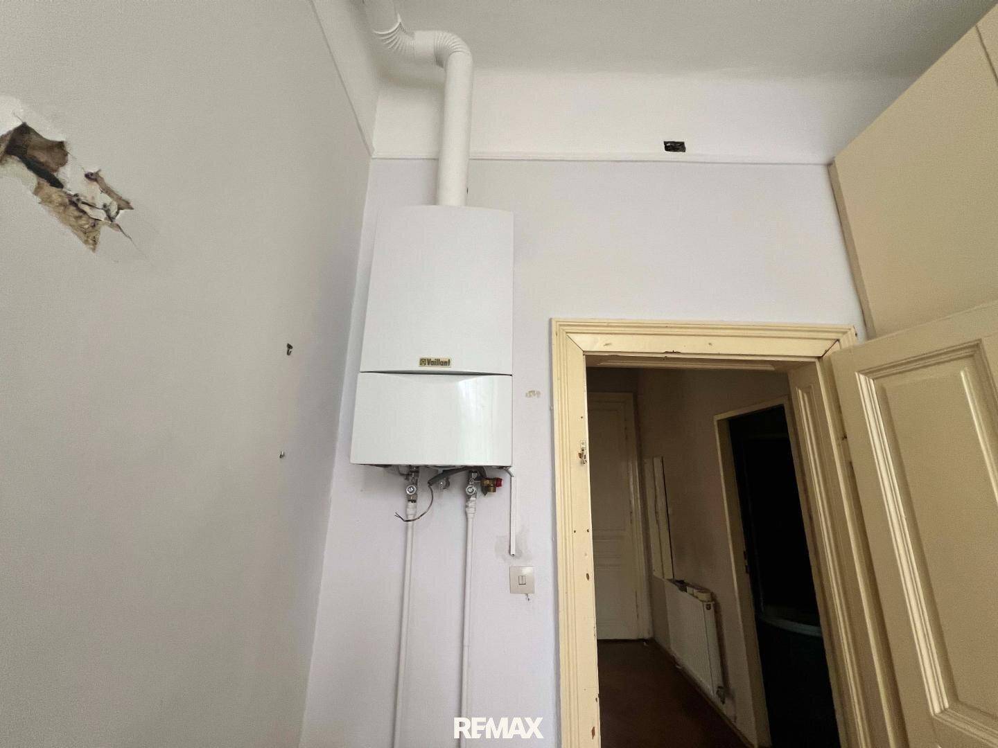 Nahaufnahme eines an der Wand montierten Heizkessels in einem einfachen Raum.
