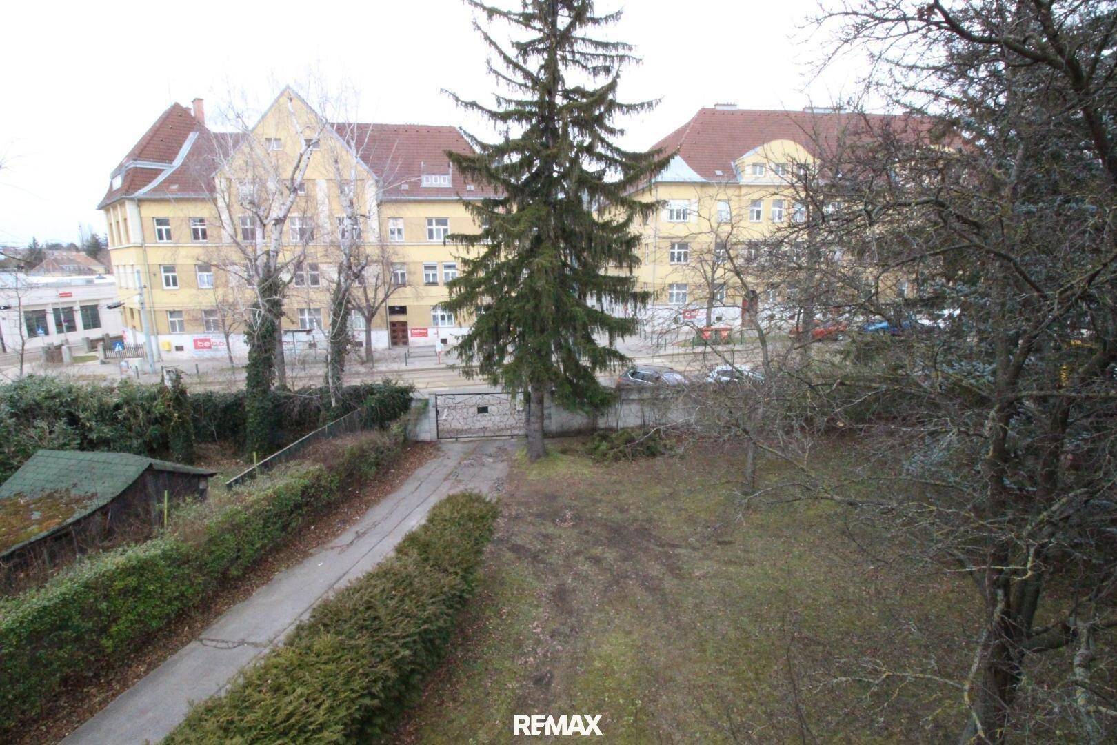 Überblick über das Grundstück mit Garten, Zufahrt und umliegenden Gebäuden in einer städtischen Umgebung.