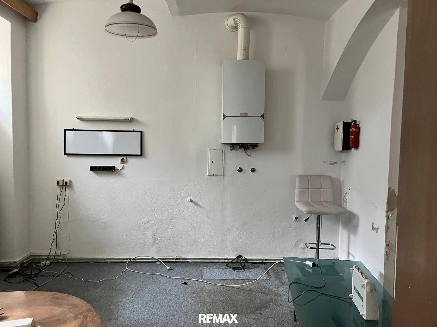 Einfacher Hauswirtschaftsraum mit Heizungsanlage, weiß gestrichenen Wänden und dunklem Teppichboden.