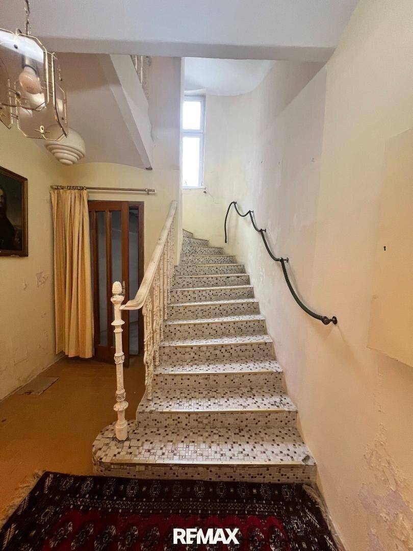Historisches Treppenhaus mit Mosaikfliesen, kunstvollem Geländer und einem Fenster im oberen Bereich.