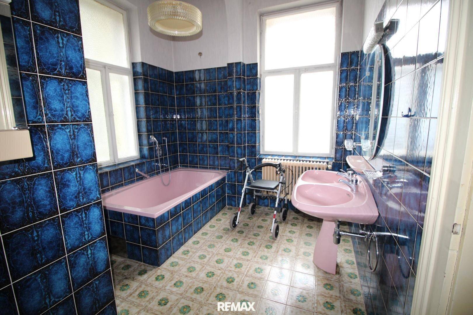 Badezimmer mit auffälligen blauen Fliesen, einer rosa Badewanne und einem passenden Doppelwaschbecken.
