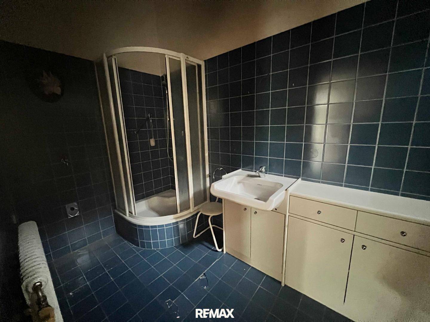 Badezimmer mit blauen Fliesen, einer Duschkabine und einem einzelnen Waschbecken.