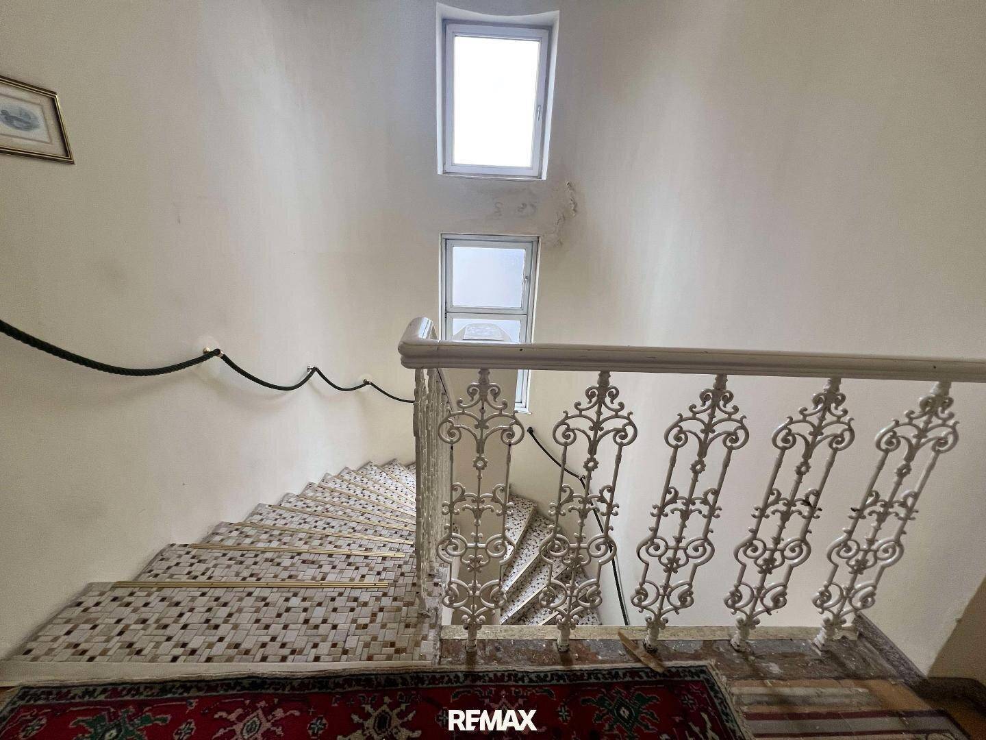 Blick von oben auf die geschwungene Treppe mit kunstvollem Geländer und Fenstern für natürliches Licht.
