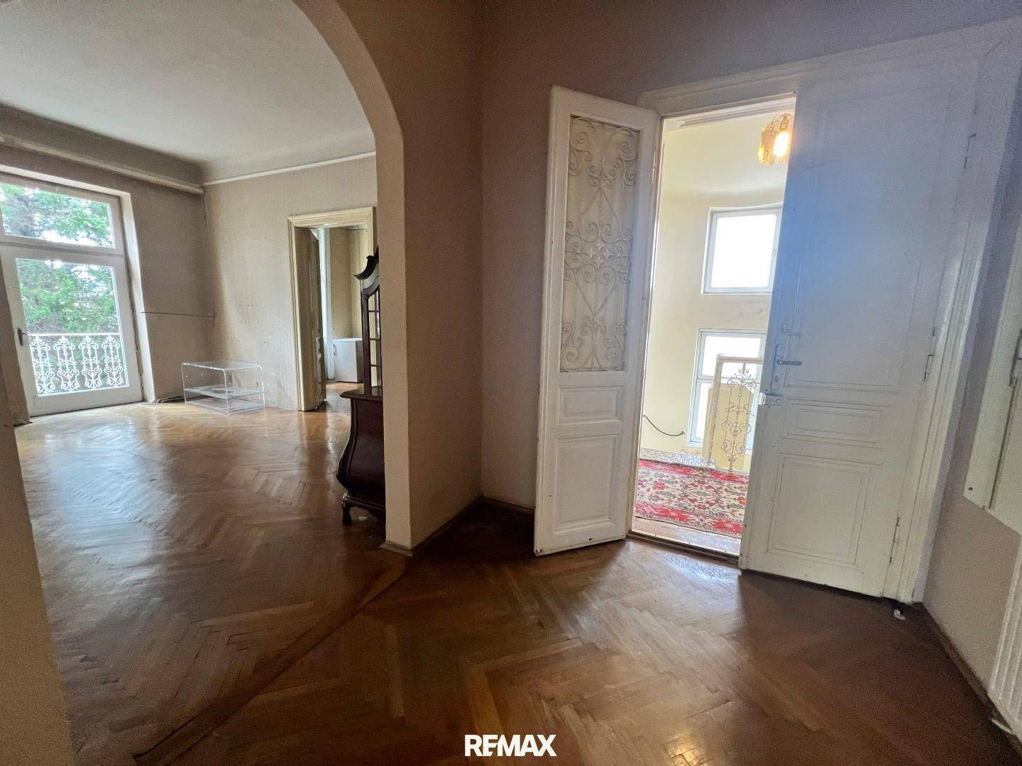 Geräumiges Wohnzimmer mit Fischgrätparkett, hohen Türen und Zugang zu einem Balkon.