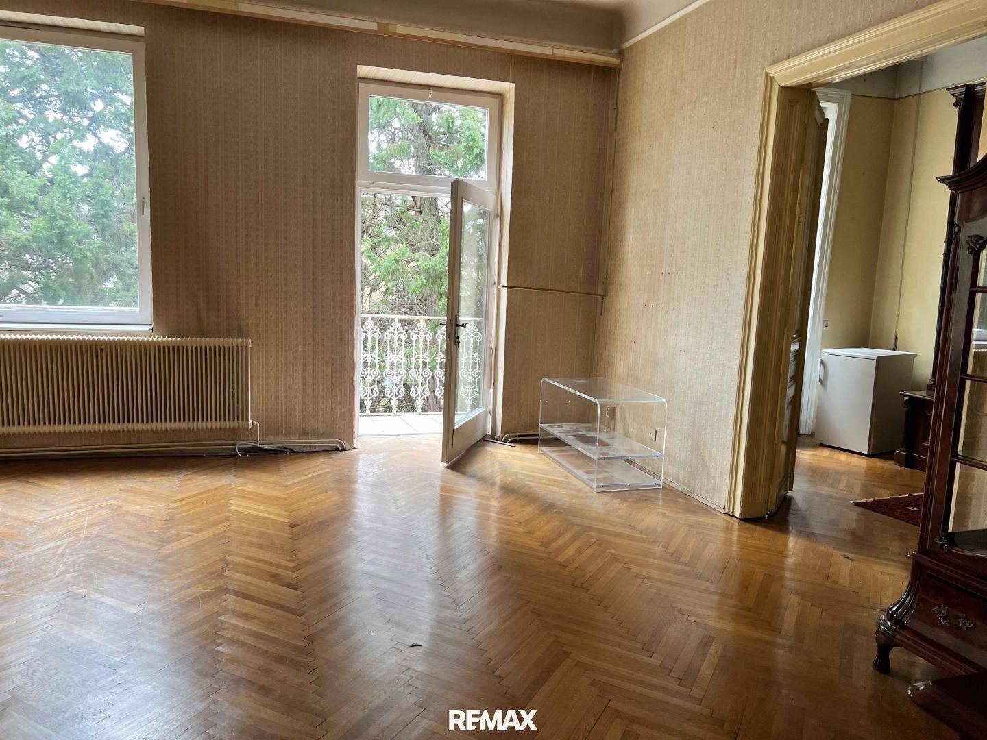 Helles Wohnzimmer mit Fischgrätparkett, großen Fenstern und direktem Zugang zu einem Balkon.