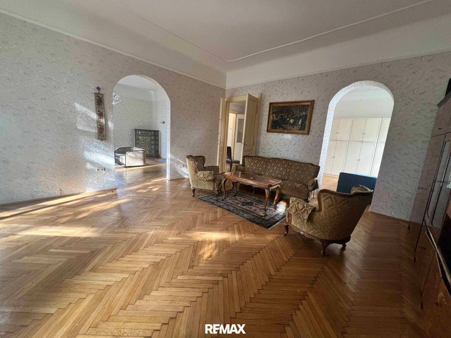 Großes Wohnzimmer mit Fischgrätparkett, traditionellen Sitzmöbeln und eleganten Bogenöffnungen.