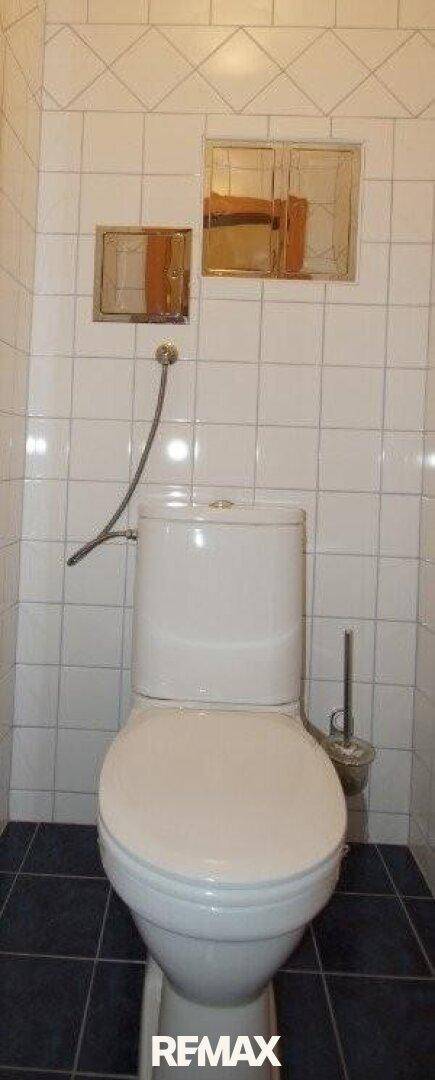 Separate Toilette mit weißen Wandfliesen und dunklem Boden.