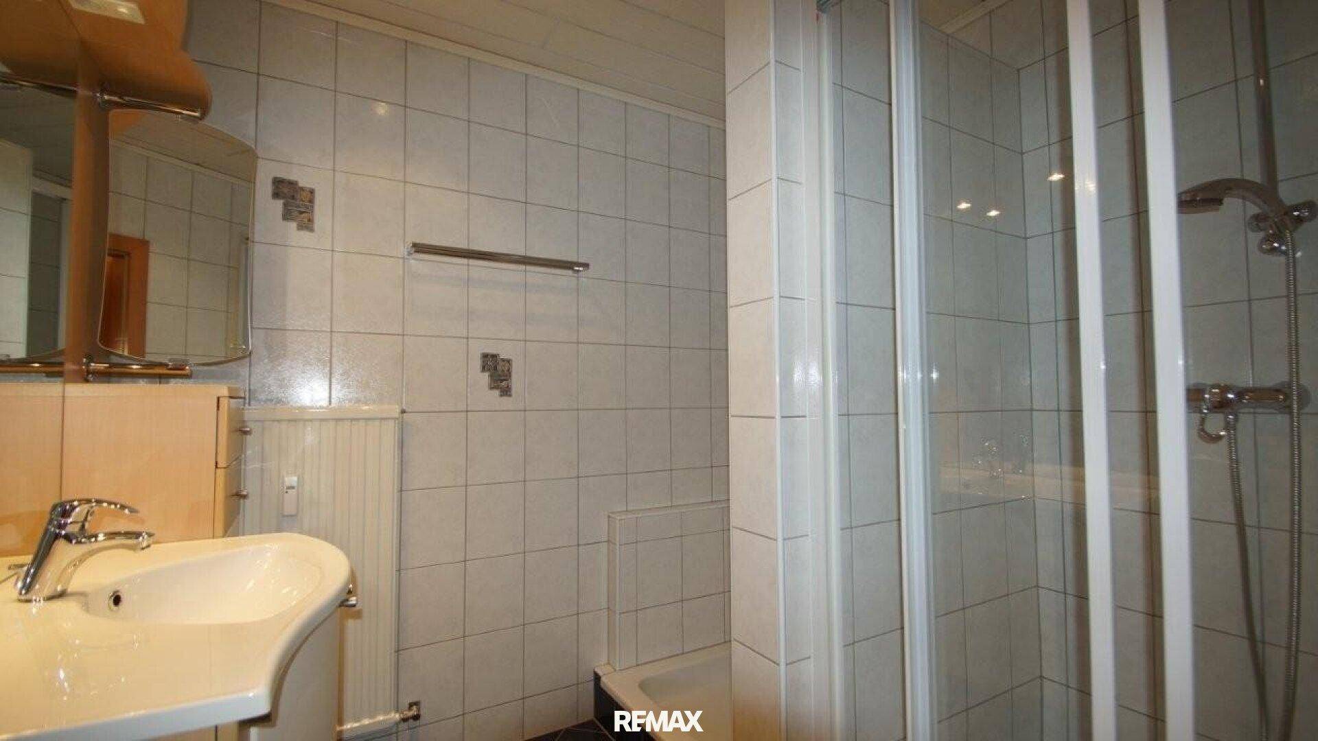 Helles Badezimmer mit Waschbecken, Spiegelschrank, Heizkörper und einer Duschkabine.