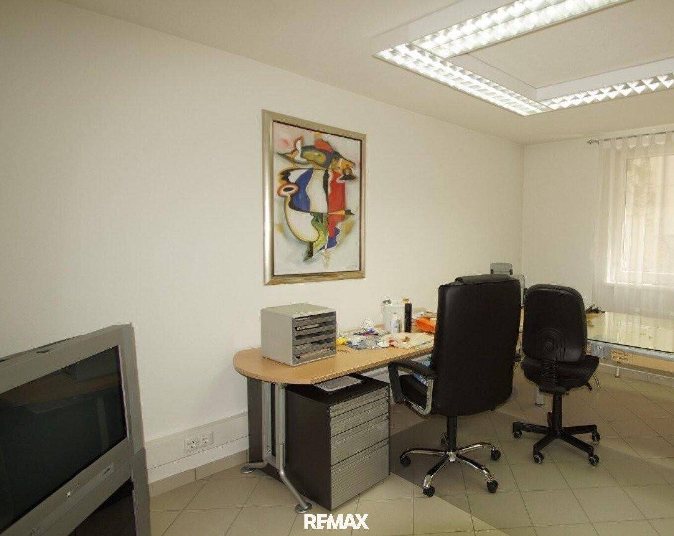 Geräumiges Büro mit Schreibtisch, Bürostuhl, Fliesenboden und einem farbenfrohen Kunstwerk.