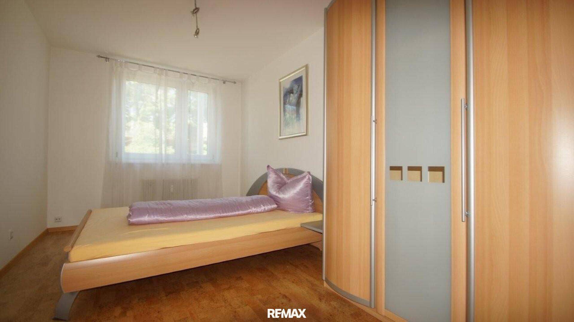 Gemütliches Schlafzimmer mit Holzbett, lila Bettwäsche und einem Kleiderschrank.