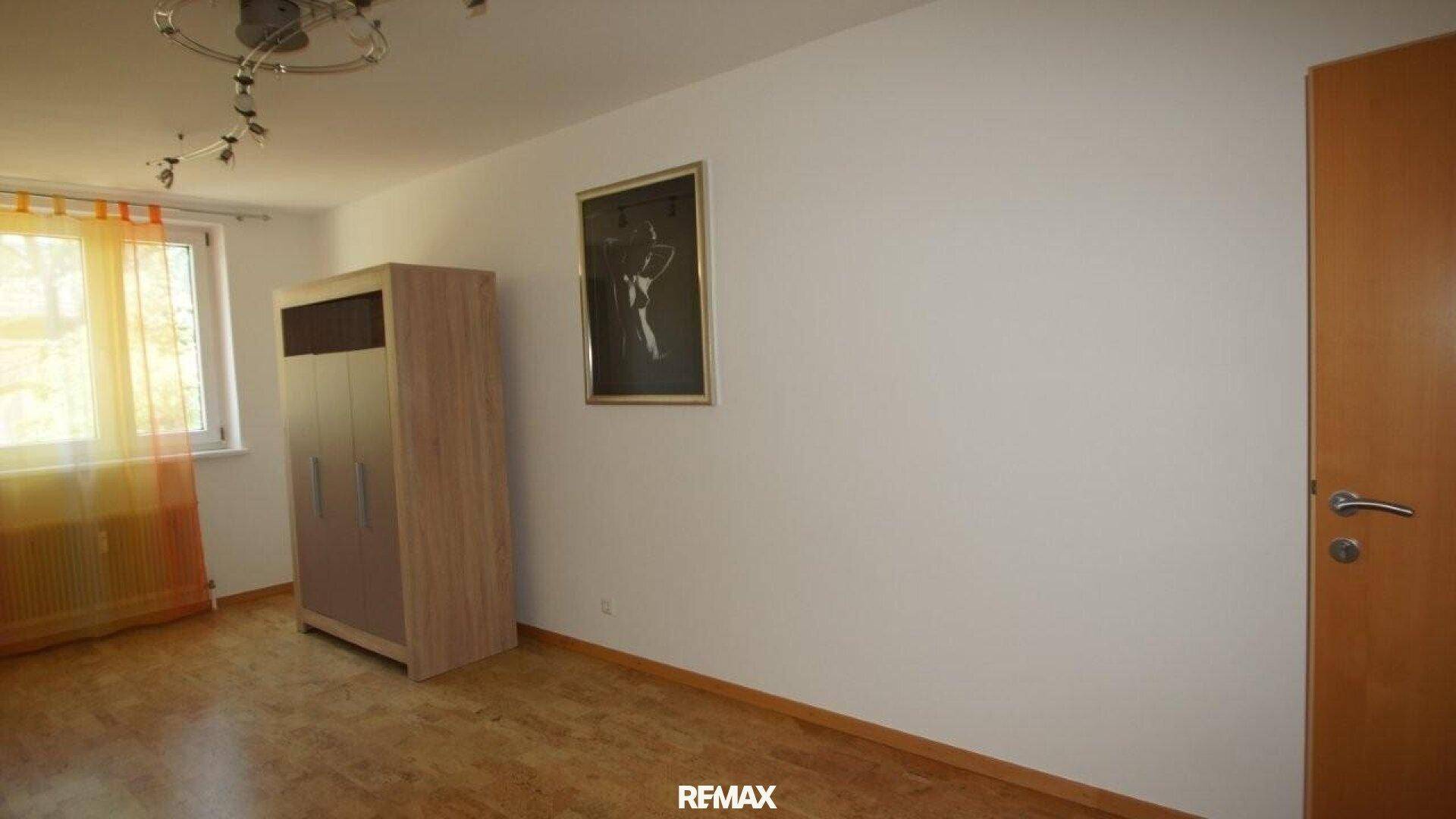 Heller Raum mit Holzfußboden, einem Kleiderschrank und einem Fenster mit orangefarbenen Vorhängen.