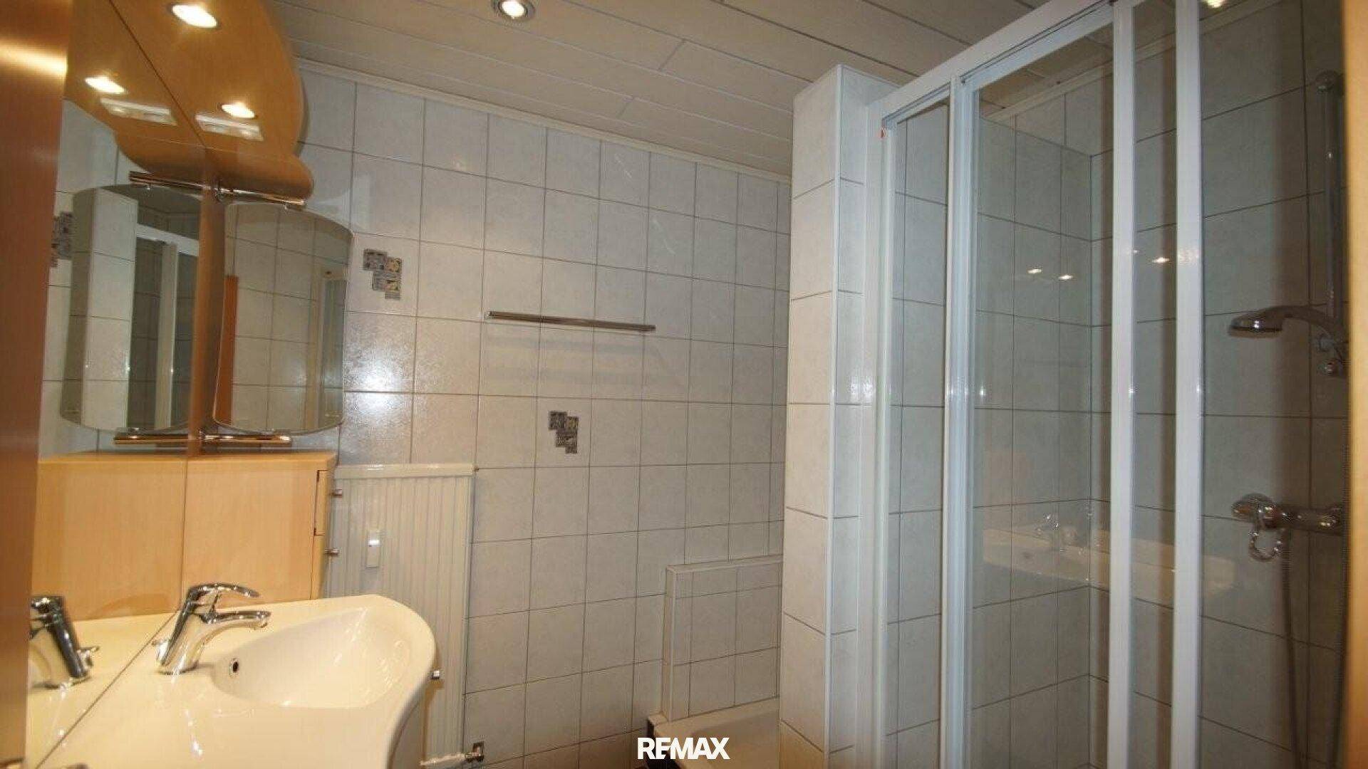 Helles Badezimmer mit Waschbecken, Spiegelschrank, Heizkörper und einer Duschkabine.
