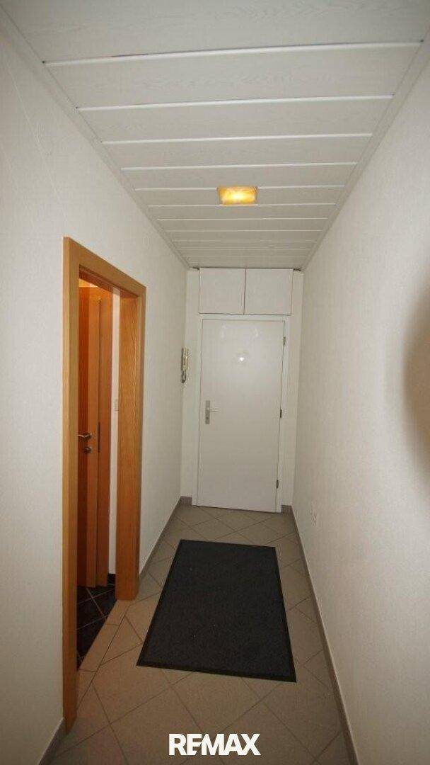 Heller Flur mit Fliesenboden, weißer Tür und Deckenbeleuchtung.