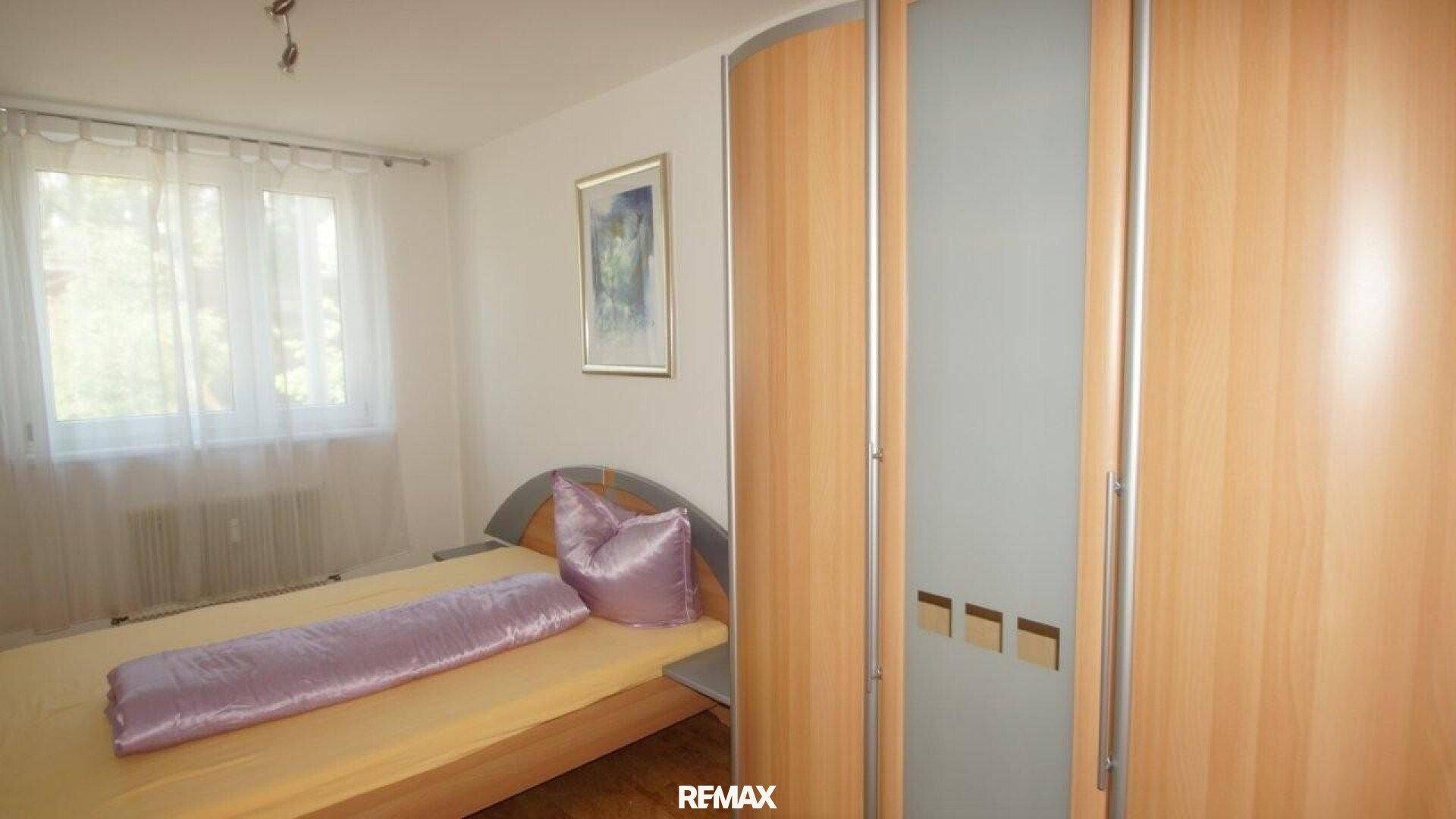 Gemütliches Schlafzimmer mit Holzbett, lila Bettwäsche und einem Kleiderschrank mit Milchglas.