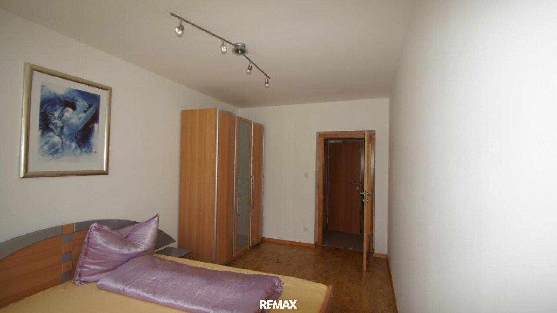 Schlafzimmer mit Holzbett, lila Bettwäsche und einem Kleiderschrank, gut beleuchtet.