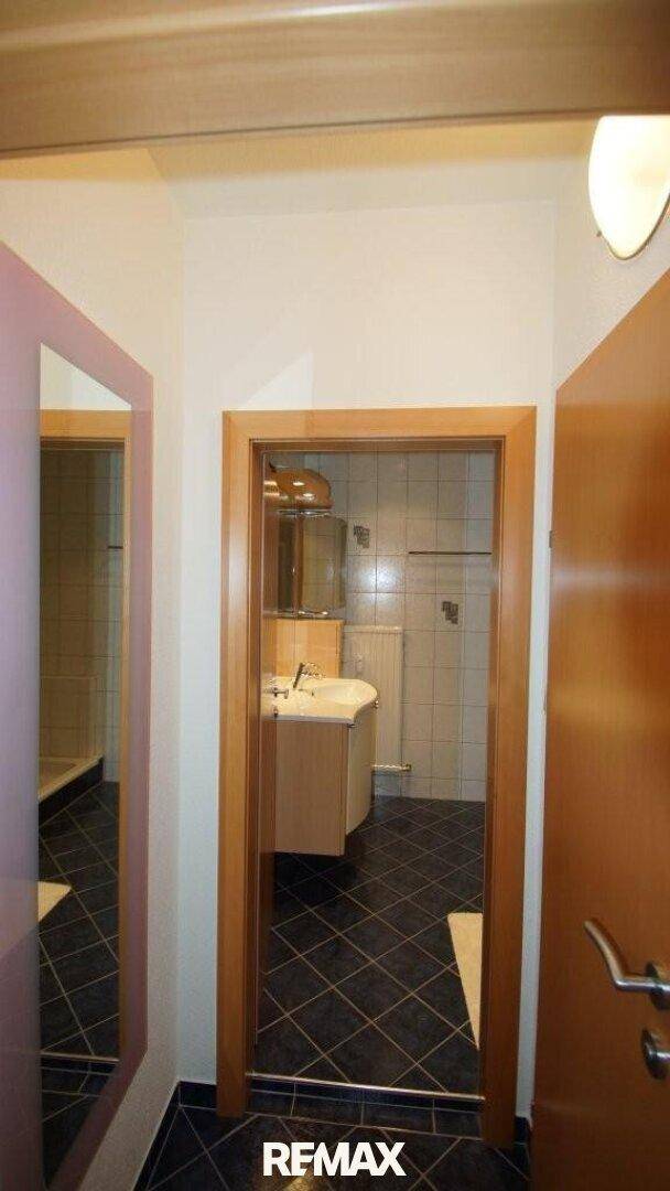 Flur mit Blick in ein Badezimmer, gekennzeichnet durch dunkle Bodenfliesen.