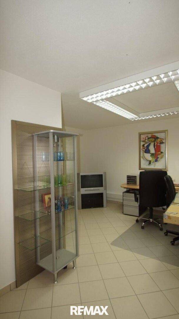 Helles Büro mit Glasvitrine, Schreibtisch und einem farbenfrohen Gemälde.