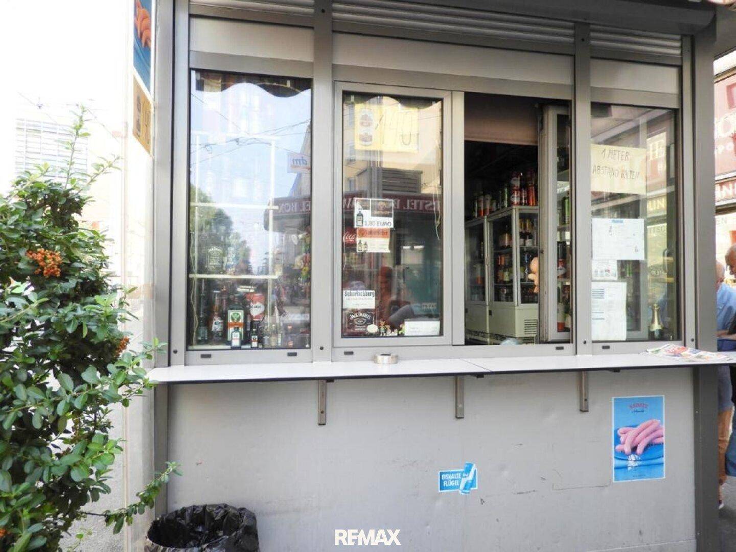 Außenansicht eines Kiosks mit Schiebefenstern und Einblick in das Sortiment an Getränken und Waren.