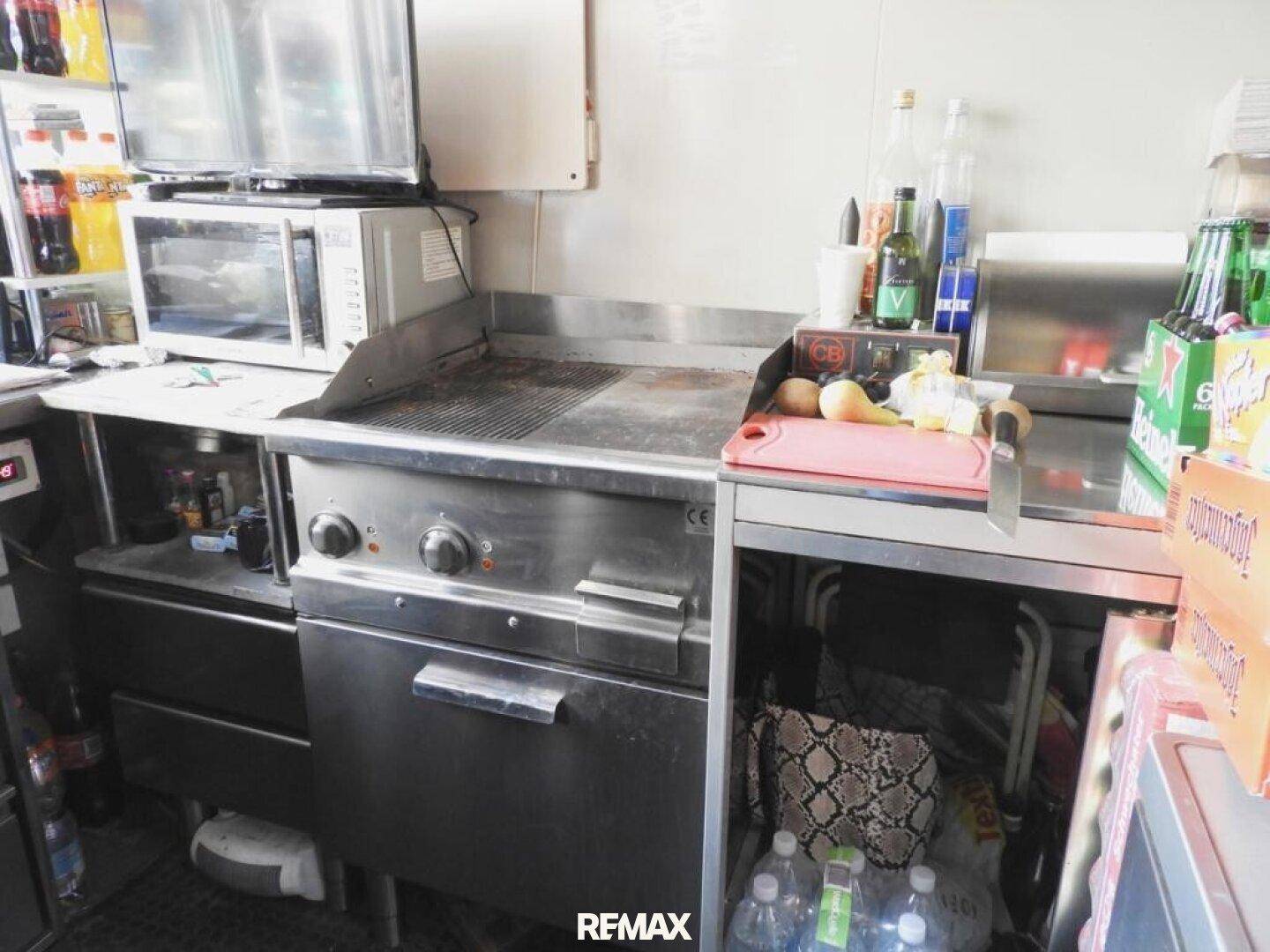 Professionelle Küchenzeile mit großem Grill, Mikrowelle und weiteren Geräten für die Zubereitung von Speisen.