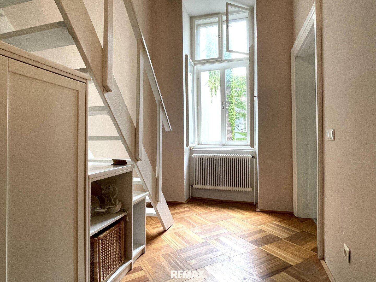 Flur mit Treppe, Fenster und integrierten Regalen unter der Treppe, Parkettboden.