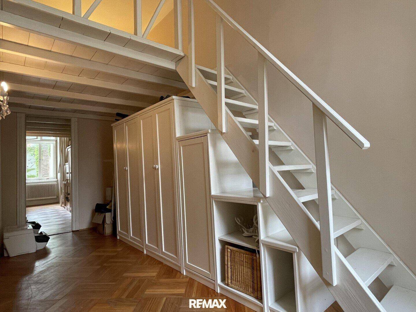 Flur mit Treppe zu einer Empore und integrierten Kleiderschränken, Parkettboden.