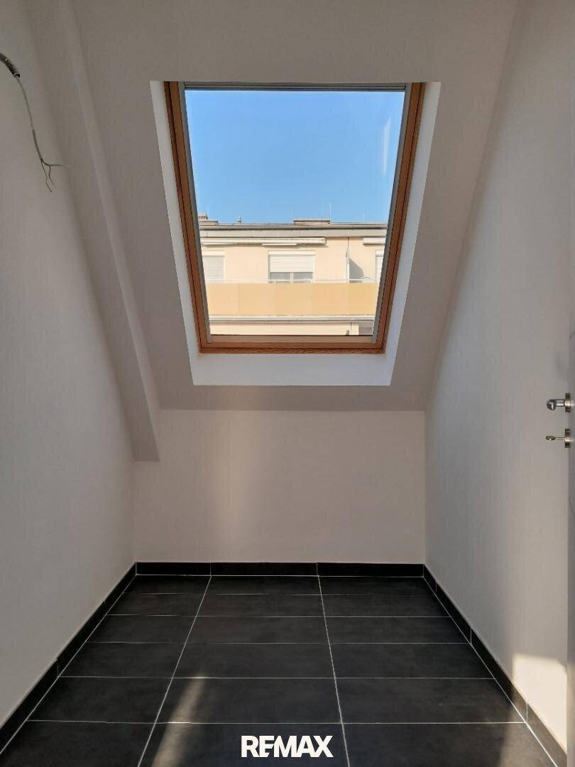 Kleiner, heller Raum im Dachgeschoss mit dunklen Fliesen und einem Dachfenster.