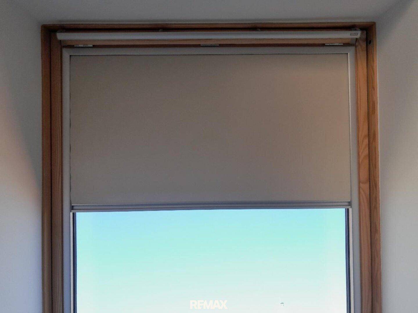 Nahaufnahme eines Fensters mit Holzrahmen und einem beigen Rollo, das für Privatsphäre sorgt.