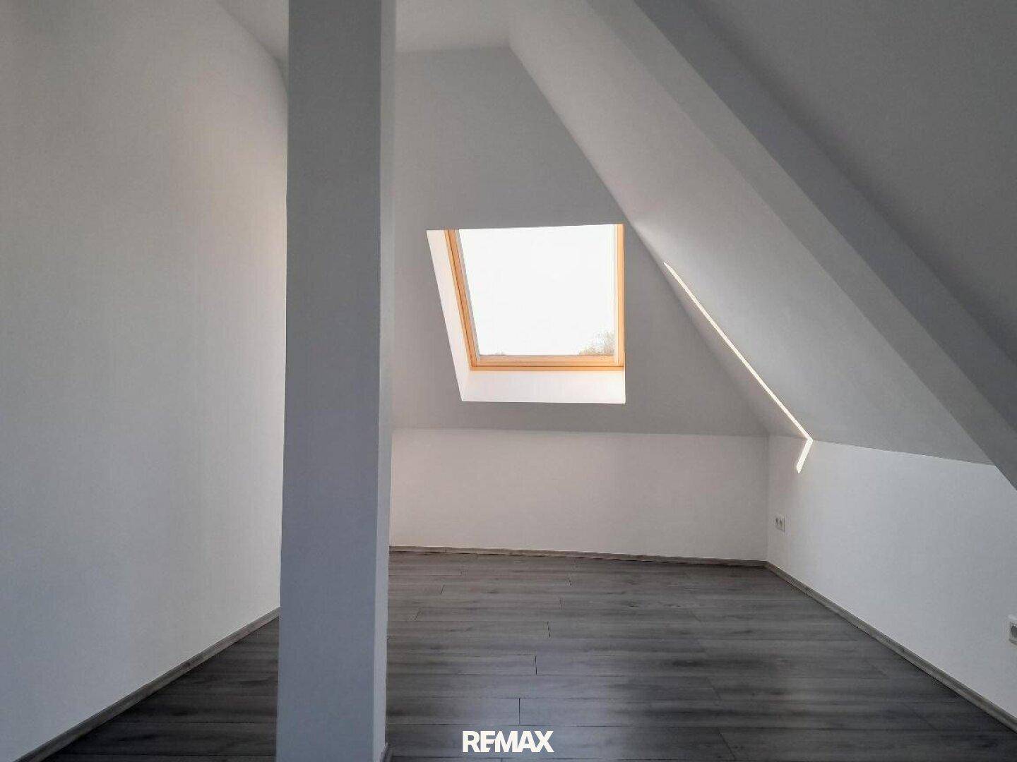 Helles Schlafzimmer im Dachgeschoss mit schrägen Wänden, Laminatboden und einem Dachfenster.