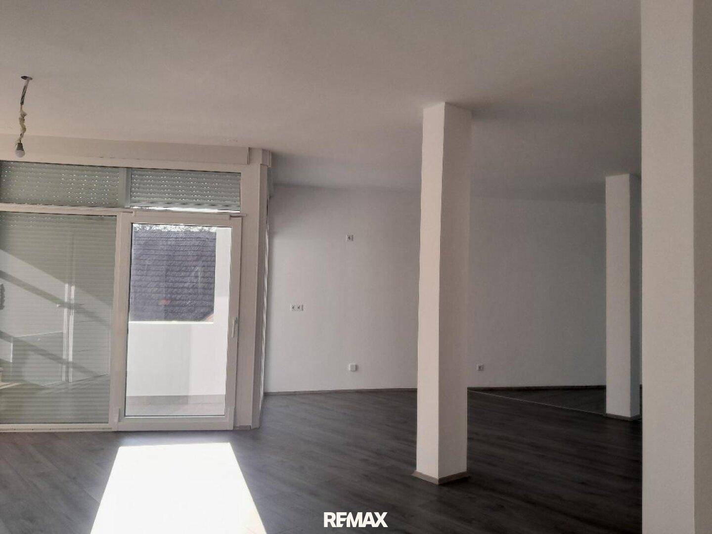 Heller, leerer Wohnbereich mit modernem Laminatboden und Zugang zu einem Balkon.