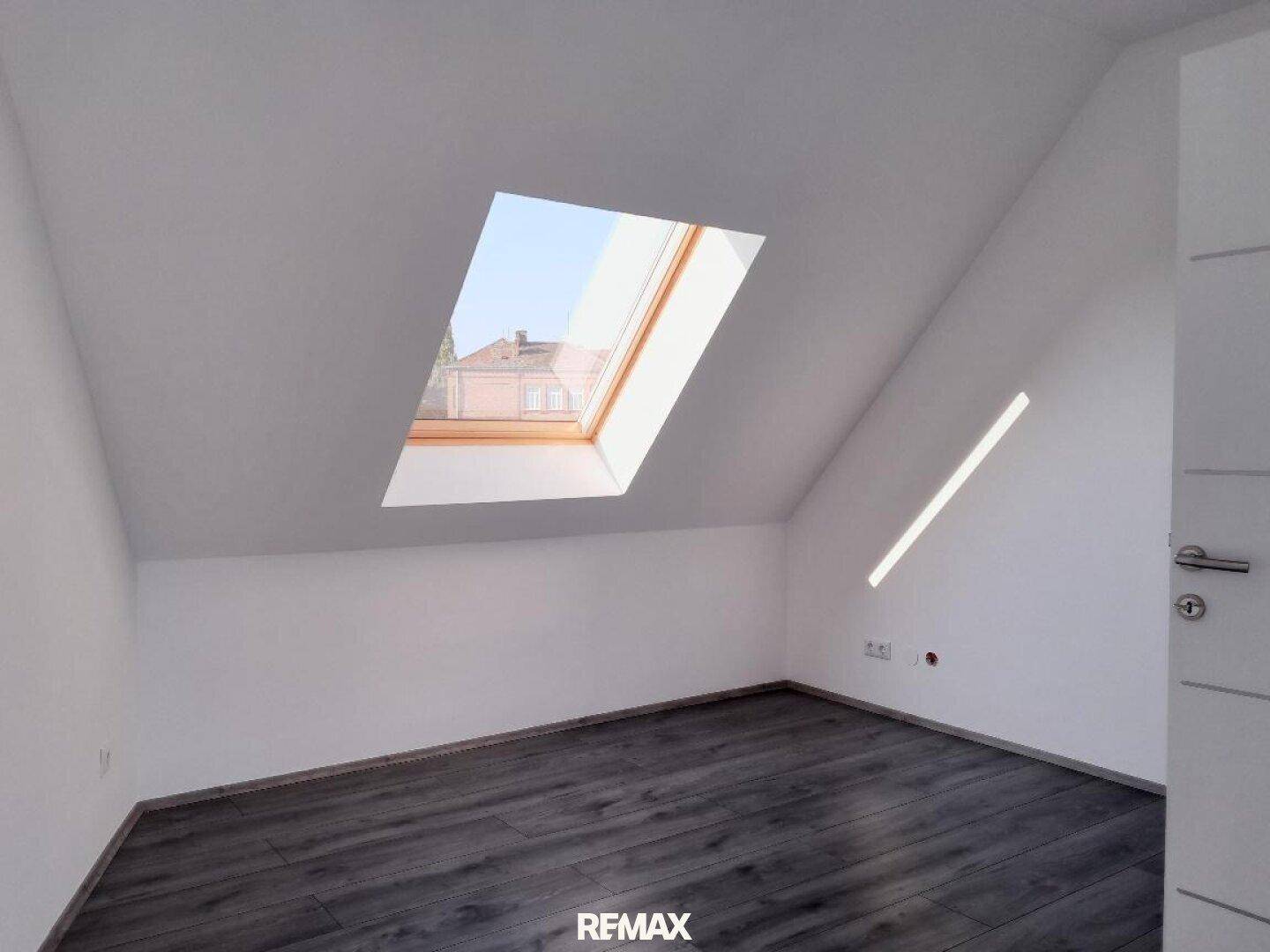 Helles Schlafzimmer im Dachgeschoss mit schrägen Wänden, Laminatboden und einem Dachfenster.