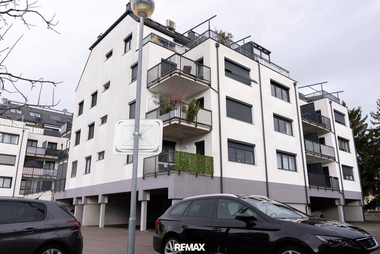 Moderne Wohnanlage mit weißen Fassaden, dunklen Fenstern und Balkonen in städtischer Umgebung.