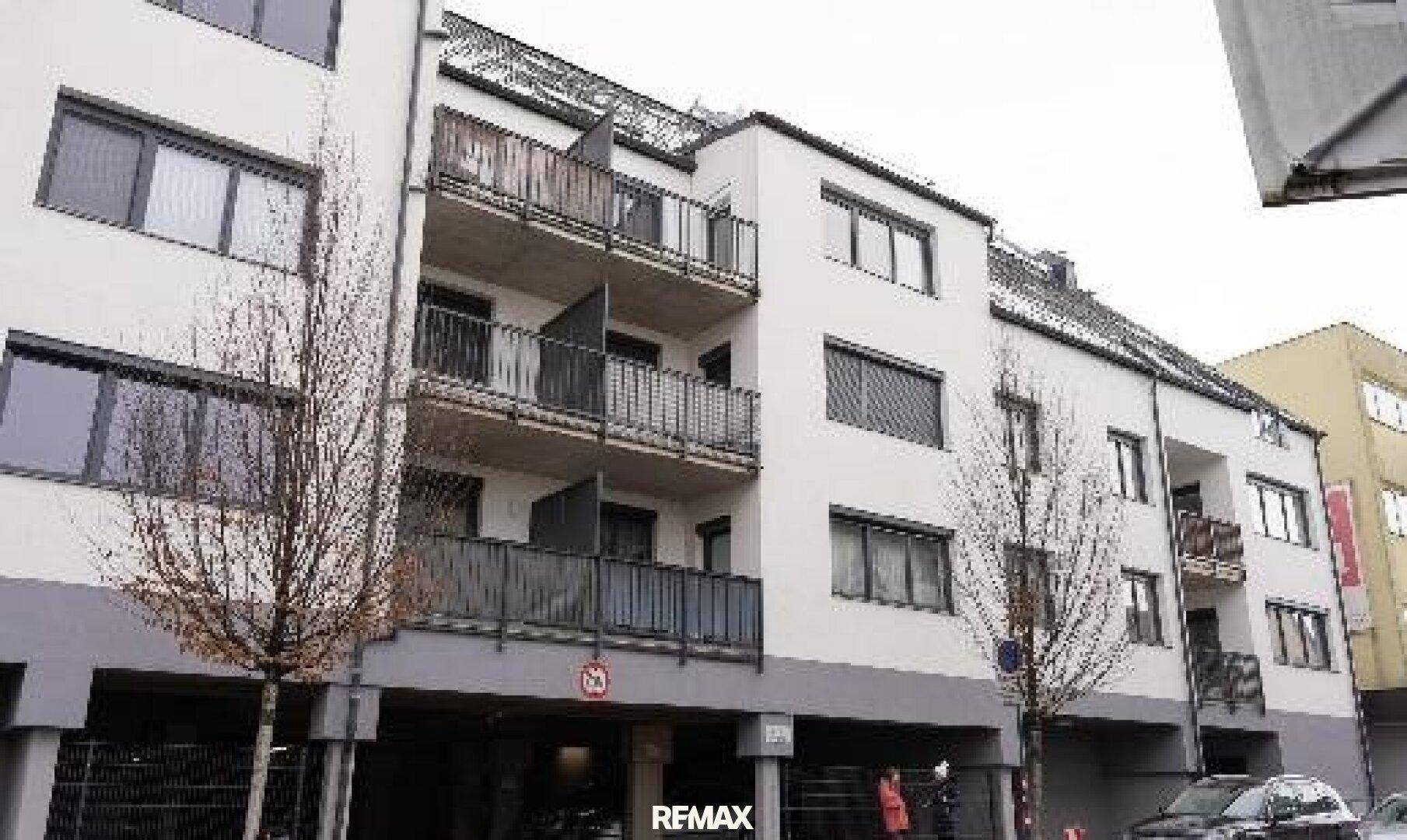 Detailansicht der modernen Fassade mit mehreren Balkonen und großen Fenstern mit Rollläden.