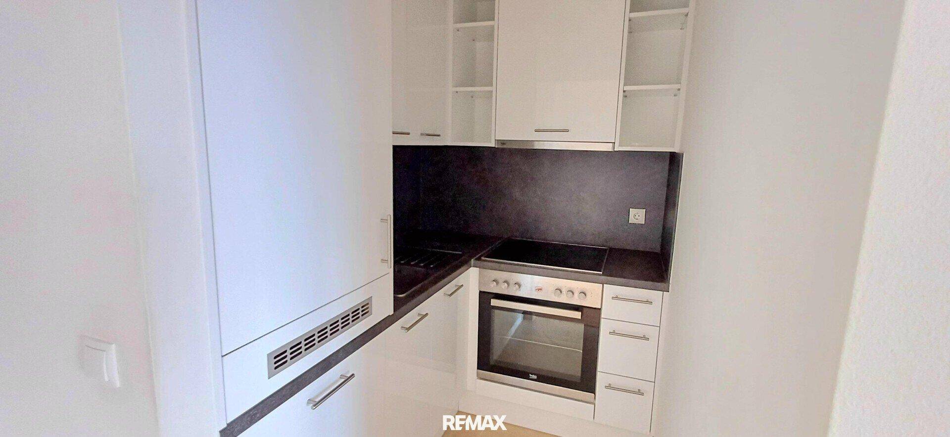 Kompakte Einbauküche mit weißen Schränken, Herd, Backofen und integriertem Kühlschrank für effizientes Kochen.