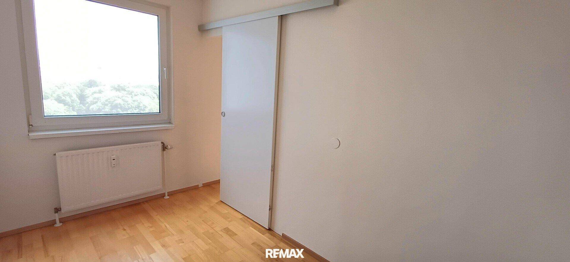 Helles Zimmer mit Holzboden, Fenster und platzsparender Schiebetür, ideal für Schlaf- oder Arbeitsbereich.
