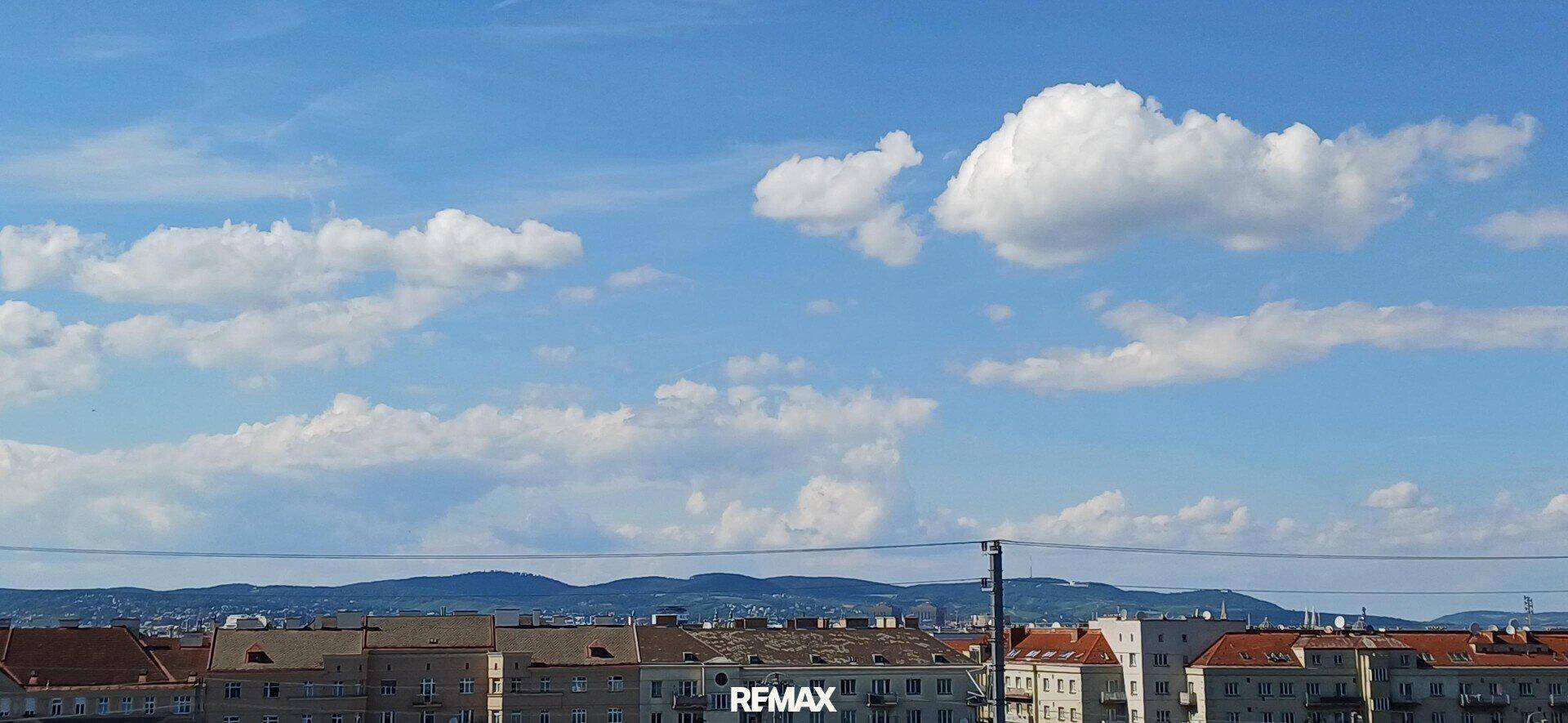 Weitblick über die Dächer der Stadt mit hügeliger Landschaft am Horizont und blauem Himmel.