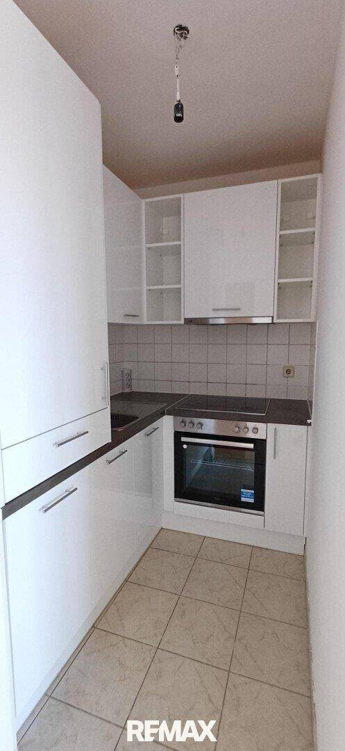 Schmale Küche mit weißen Einbauschränken, Herd und Fliesenboden in hellem Design.